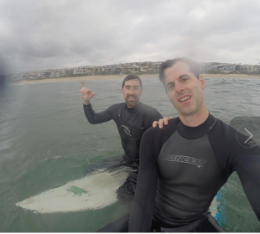 Two men in wetsuits paddling on boards in the ocean